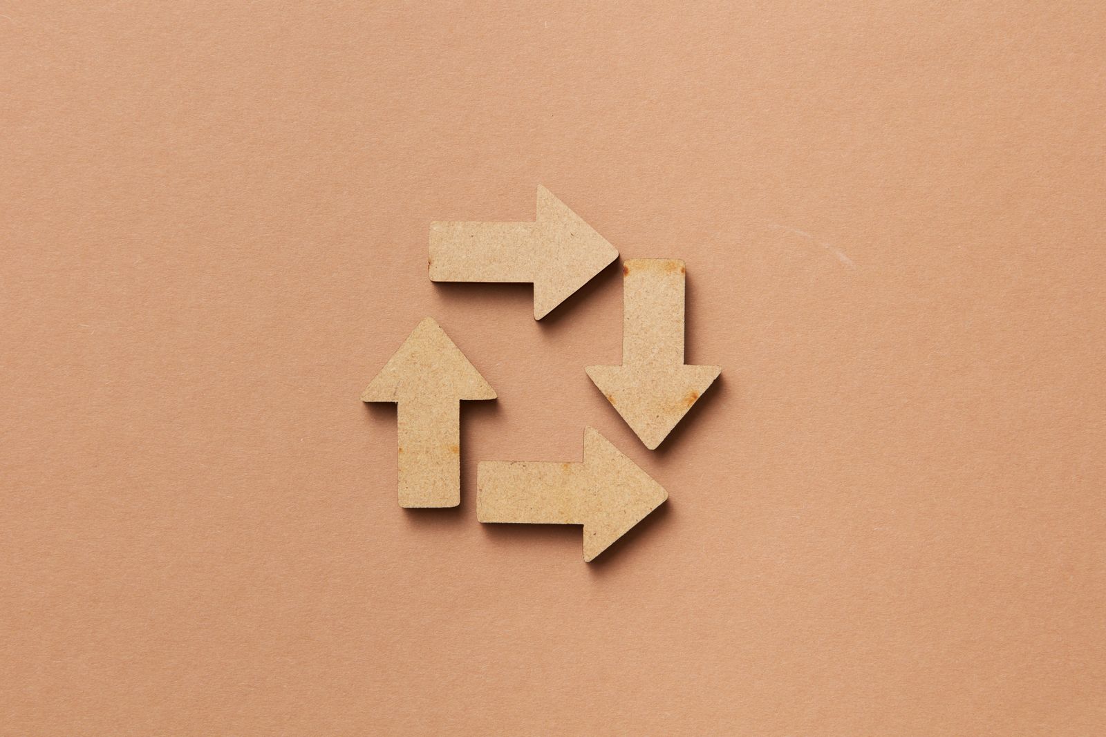 Símbolo de reciclaje formado por flechas de material natural sobre fondo neutro, que ilustra la economía circular y el ciclo de vida de los materiales