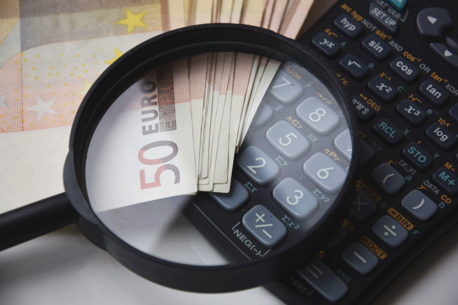 Billetes de 50 euros vistos a traves de una lupa junto a una calculadora cientifica: anali