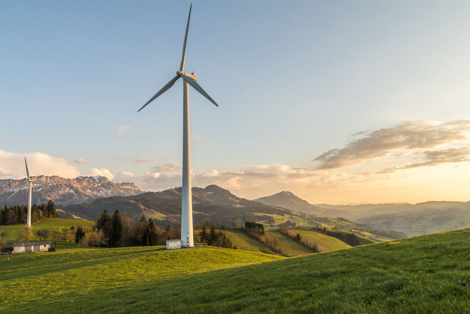 Aerogenerador en una colina verde con montañas al fondo, energía eólica en un entorno natural